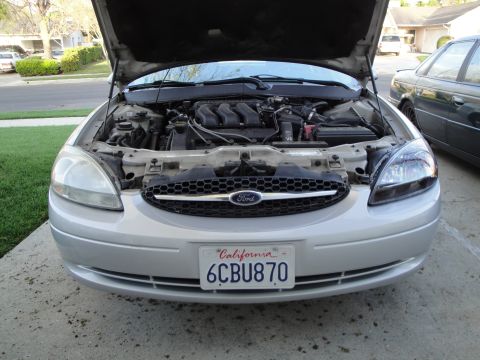 2003 Ford Taurus - Front view of a silver Ford Taurus, hood up, revealing the engine compartment and grille.