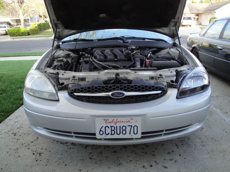 Silver Ford Taurus with hood open, showing engine and front grille with Ford logo. California license plate 6CBU870