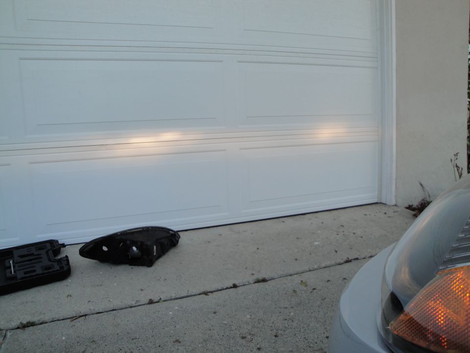 Black headlight assembly and mounting bracket on concrete in front of a white garage door