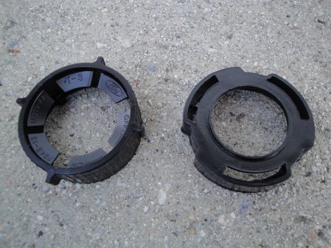 2003 Ford Taurus - Two black plastic headlight retainer rings are shown on a concrete surface. One ring has a Ford logo and part numbers visible.
