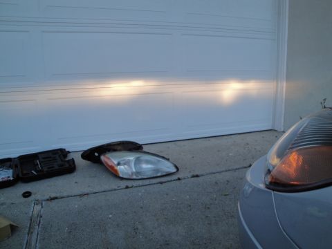 2003 Ford Taurus - Two headlights are on the ground, one is installed on a car. A tool kit is nearby.