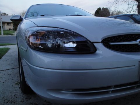2003 Ford Taurus - The front grille and headlights of a silver sedan are visible, with another vehicle in the background.