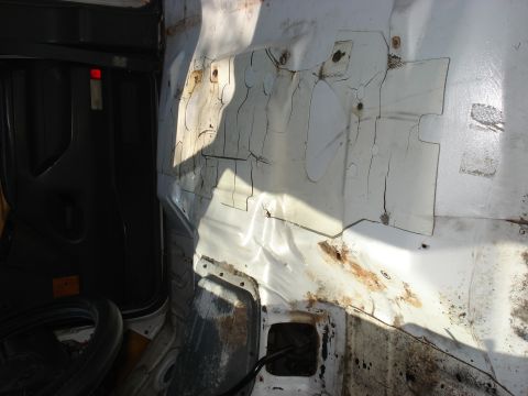 1992 Ford C-350 (Centurion Conversions) - Stripped truck cab interior with the carpet and seats removed, showing a white-painted sheet-metal floor pan with surface rust along the se…