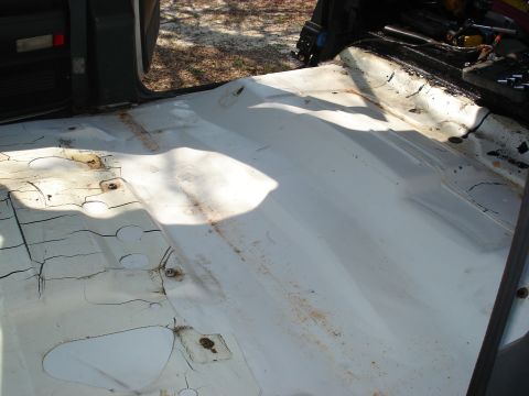 1992 Ford C-350 (Centurion Conversions) - Close view of a stripped truck cab floor pan painted white, showing the transmission tunnel, seat-mount studs, drain plugs and cracked, pee…