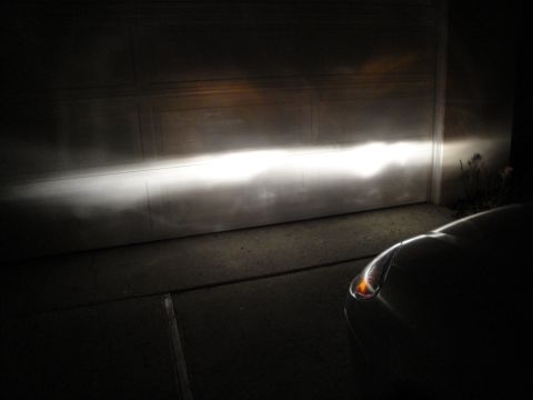 2003 Ford Taurus - Headlight beam projected onto a garage door at night. A car's front corner is visible.