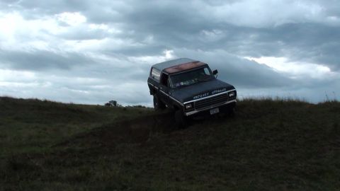1978 Ford Bronco - A 1978 Ford Bronco navigates a grassy incline under a dramatic, cloudy sky.