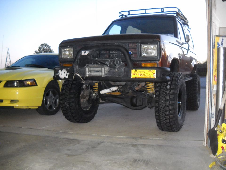 1986 Ford Bronco II with winch and roof rack parked next to a yellow Ford Mustang