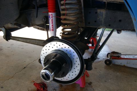 1978 Ford Bronco - Close-up view of a vehicle's front suspension system, a disc brake rotor and a red shock absorber.