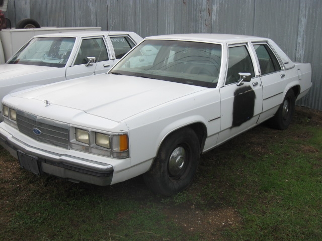 1991 Ford Crown Victoria LTD sedan, white, with black patch on driver's door, parked next to another white sedan