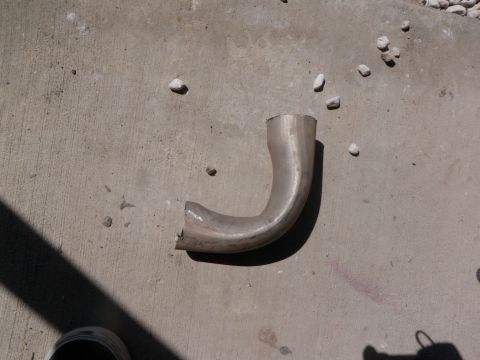 1982 Ford Bronco - A bent exhaust pipe section lies on a concrete surface with scattered small rocks.