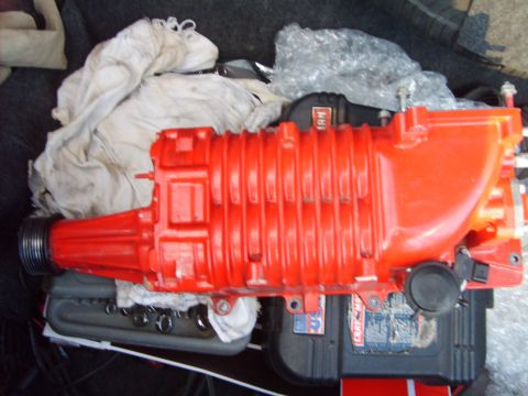 1993 Ford Crown Victoria - An Eaton-style roots supercharger painted bright red-orange, resting on its side atop tool cases and shop rags with the black serpentine pu…