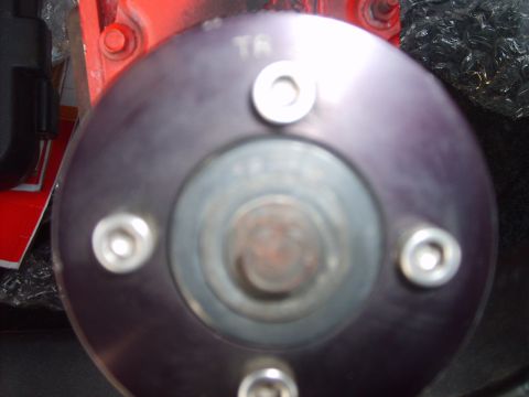 1993 Ford Crown Victoria - Very close view straight onto the face of a supercharger drive pulley, the smooth disc bolted down by four hex-head fasteners around a cent…