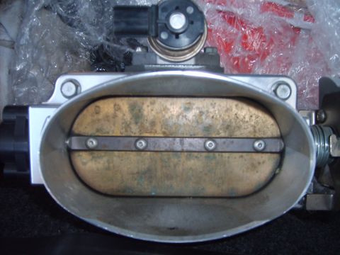 1993 Ford Crown Victoria - Head-on view into the bore of a large oval single-blade throttle body, with the discolored brass throttle plate closed and secured by four…