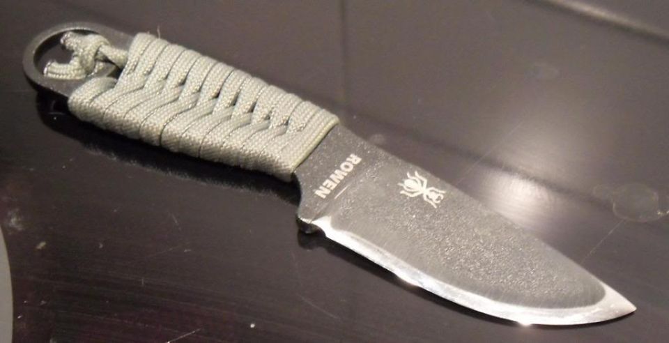 Knife with paracord-wrapped handle and a spider logo on the blade. Text reads ROWEN