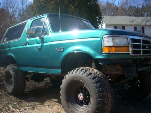 1996 Ford Bronco - A teal Ford Bronco with a lifted suspension and aggressive tires sits outdoors on a dirt lot.