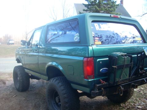 1996 Ford Bronco - A green Ford Bronco with off-road tires and a rear-mounted jerry can is parked outdoors.