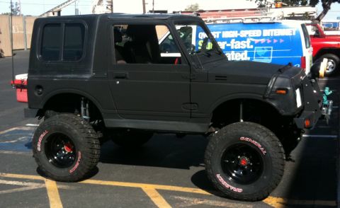 1987 Suzuki Samurai - This modified SUV is parked in a lot with other vehicles visible in the background.