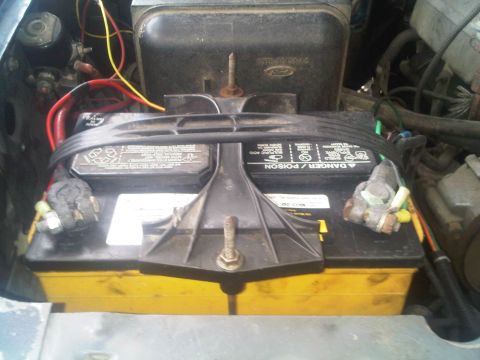 1986 Ford Bronco - The engine bay shows a yellow-cased battery with visible wiring and a Ford logo on a plastic cover.