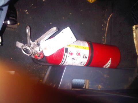 1986 Ford Bronco - A red fire extinguisher is visible on the floor of a vehicle, with instructions printed on its side.
