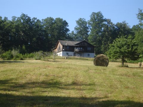 1989 Ford Bronco - A mowed hay field with round bales in the foreground leads up to a two-story barn-style house with weathered wood siding and a white lower…