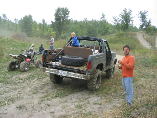 1986 Ford Bronco rear view with ATV and people in a wooded area