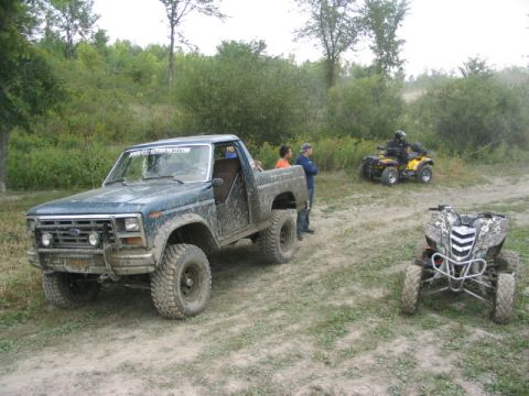 1986 Ford Bronco - A muddy 1980 Ford pickup truck is parked on a dirt path with two ATVs in the background.