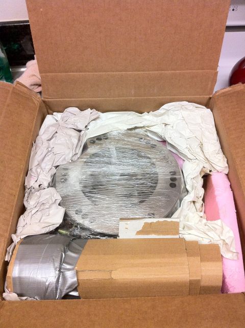 1989 Ford Bronco - A transfer case adapter, likely for a Ford Bronco, is shown packed in a cardboard box with protective wrapping.