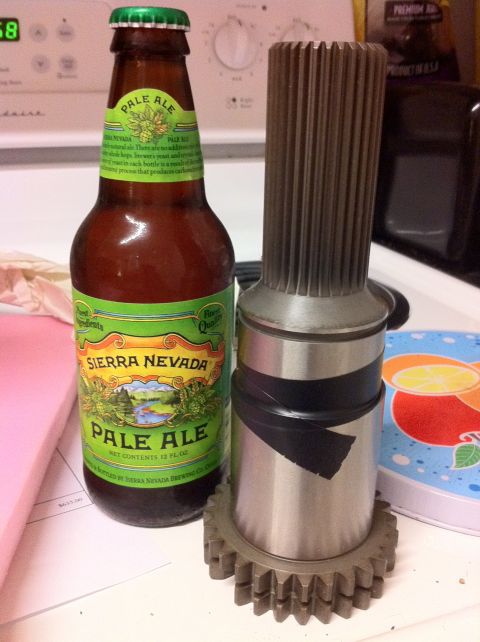 1989 Ford Bronco - A metal shaft with splines and a gear, possibly a transmission part, is shown next to a beer bottle.