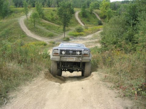 1986 Ford Bronco - A lifted Ford truck navigates a challenging off-road course with winding dirt paths.