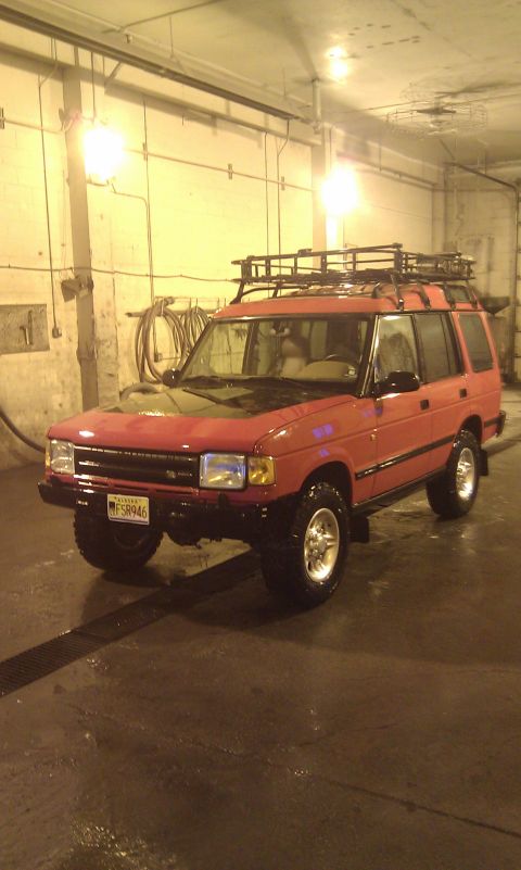 1990 Chevrolet Suburban - This red Land Rover Discovery is parked inside a garage, equipped with a roof rack.