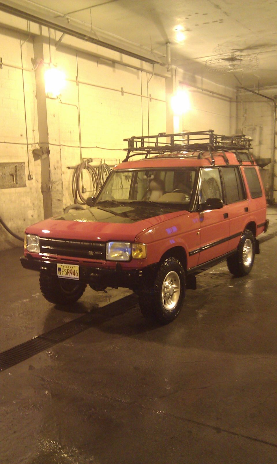 Red Land Rover Discovery with roof rack parked indoors, license plate FSR946