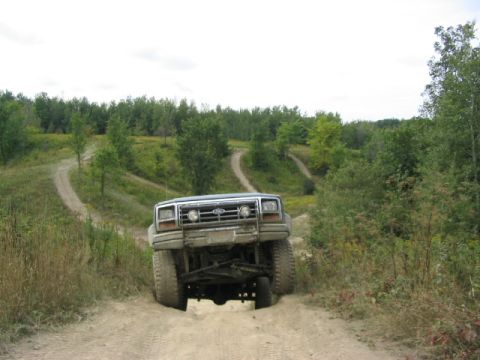 1986 Ford Bronco - A gray Ford Bronco navigates a winding dirt path through a wooded area with a lifted suspension.