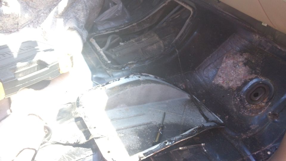 Interior of a vehicle with torn upholstery and exposed metal, showing the wheel well and floor pan