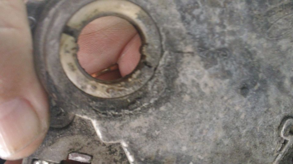 Hand pointing at a worn bore in a greasy metal automotive housing