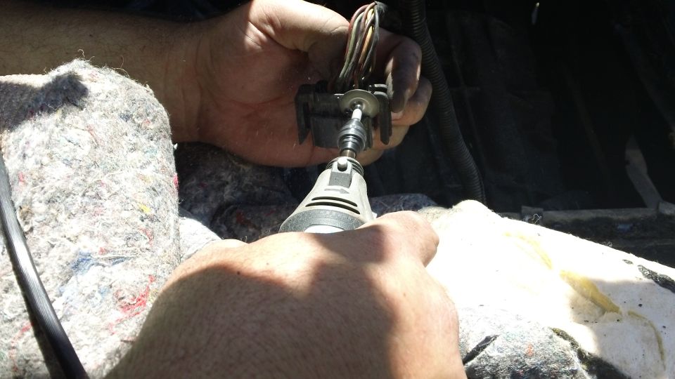 Hands using a Dremel tool to modify an electrical connector with wires
