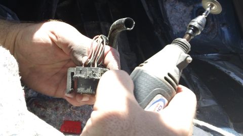 1994 Ford Bronco - A person is using a rotary tool to work on a vehicle's wiring harness.