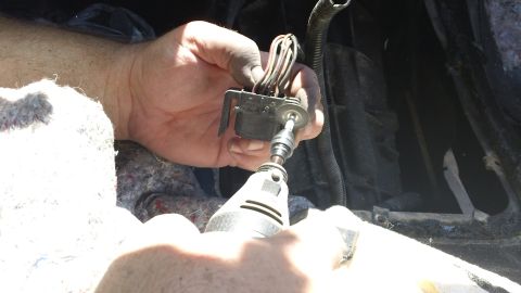 1994 Ford Bronco - Close-up of a hand working on a vehicle's wiring harness connector with a rotary tool.