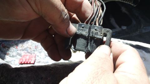 1994 Ford Bronco - Close-up of a damaged vehicle wiring harness connector being handled by two hands, with frayed wires visible.