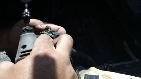 1994 Ford Bronco - Hands use a rotary tool to work on a black car part.