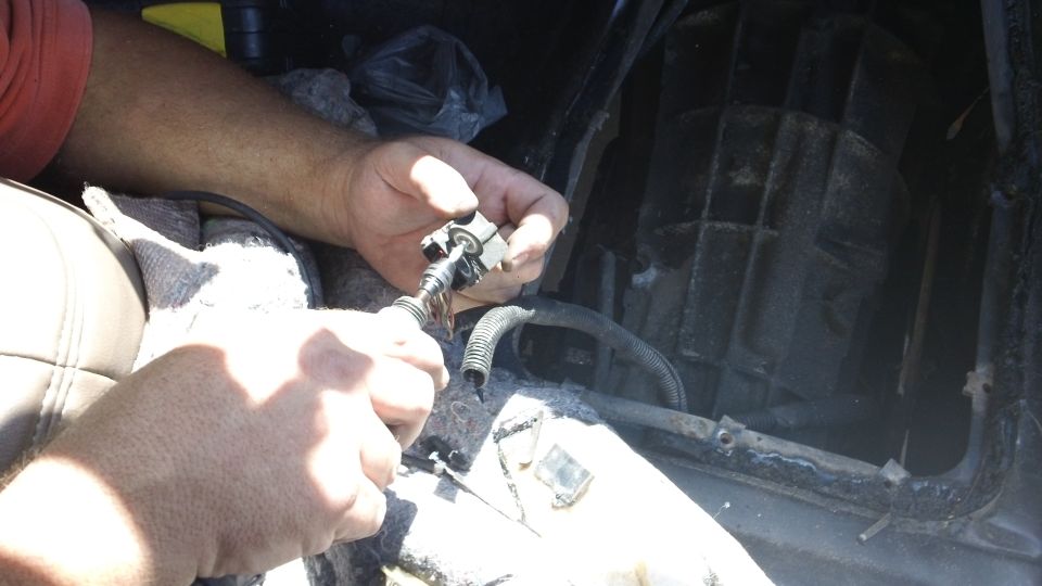 Hands working on a car's interior component, possibly a sensor or wiring harness
