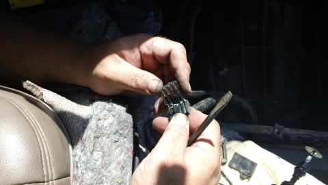 1994 Ford Bronco - Hands work a small pick tool into a multi-pin black electrical connector, releasing the terminals from the plug body. A partially disassemb…