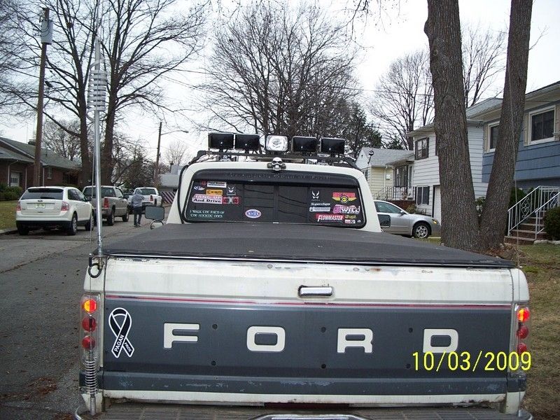 Rear of two-tone white and gray Ford pickup with tonneau cover, roof light bar and sticker-covered rear window