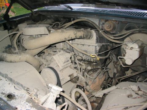 1986 Ford Bronco - The engine bay is filled with dusty components and various hoses, obscuring specific details.