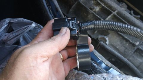 1994 Ford Bronco - Close-up of a hand holding a black electrical connector attached to a wiring harness.