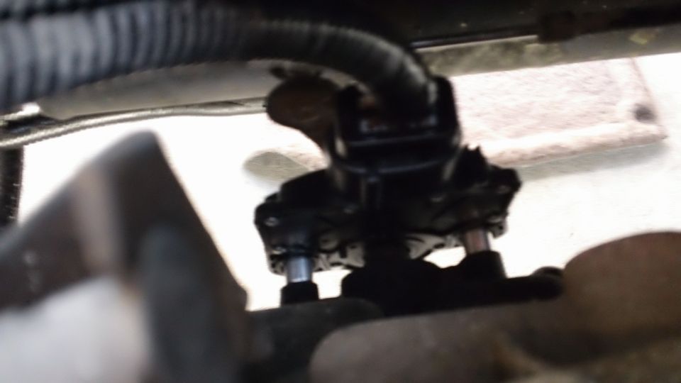 Close-up of black automotive component with silver bolts, under a ribbed black cable