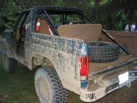1986 Ford Bronco - Mud-covered 1986 Ford Bronco with spare tire and shovel in the bed.