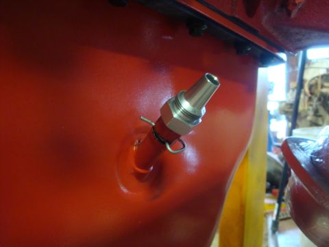 1989 Ford Bronco - Close-up of a red engine block with a metal fitting and hose clamp.