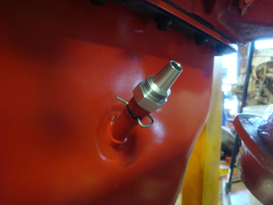 Red engine block with a metal fitting attached by a hose clamp and cotter pin
