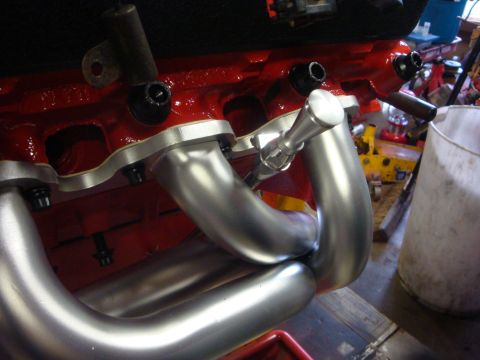 1989 Ford Bronco - Shiny exhaust manifold installed on a red engine block in a workshop setting.