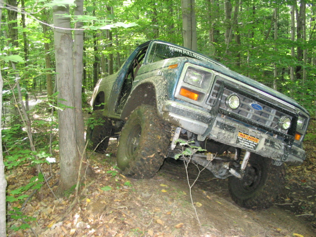 Green Ford Bronco off-roading in a forest, tilted on a dirt path